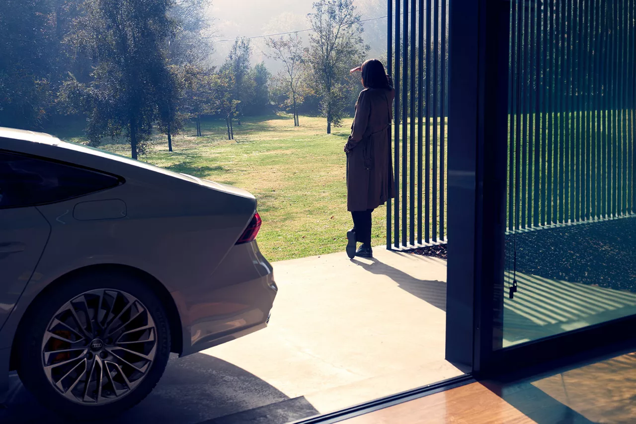 Eine Frau lehnt an einem Fenster und schaut hinaus. Hinter ihr steht ein weißer Audi A7