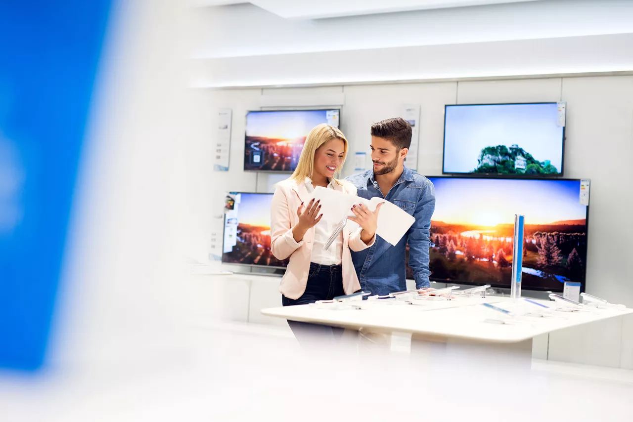 Zadowolona para w sklepie RTV, przymierzająca się do zakupu telewizora