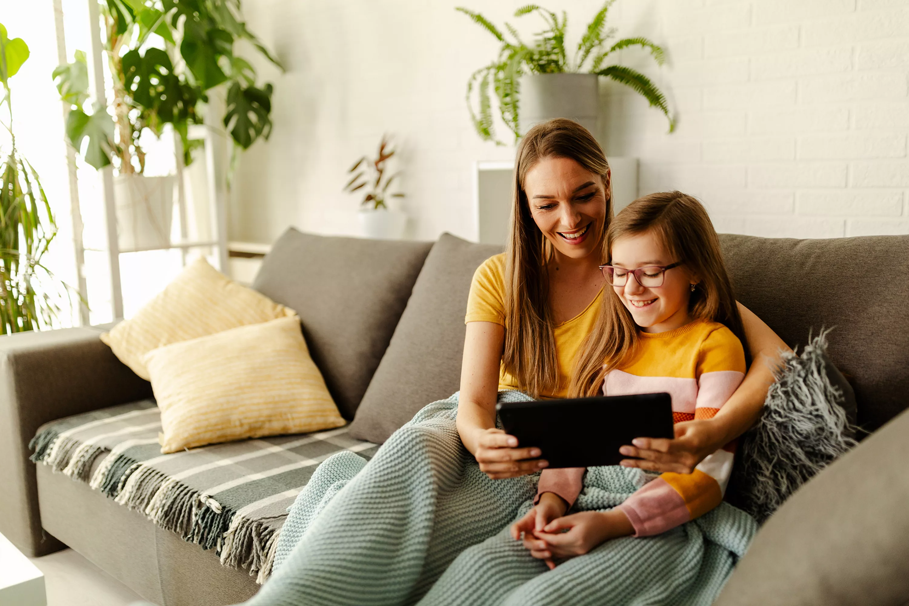 Wesoła mama z córka korzystają z tabletu na kanapie