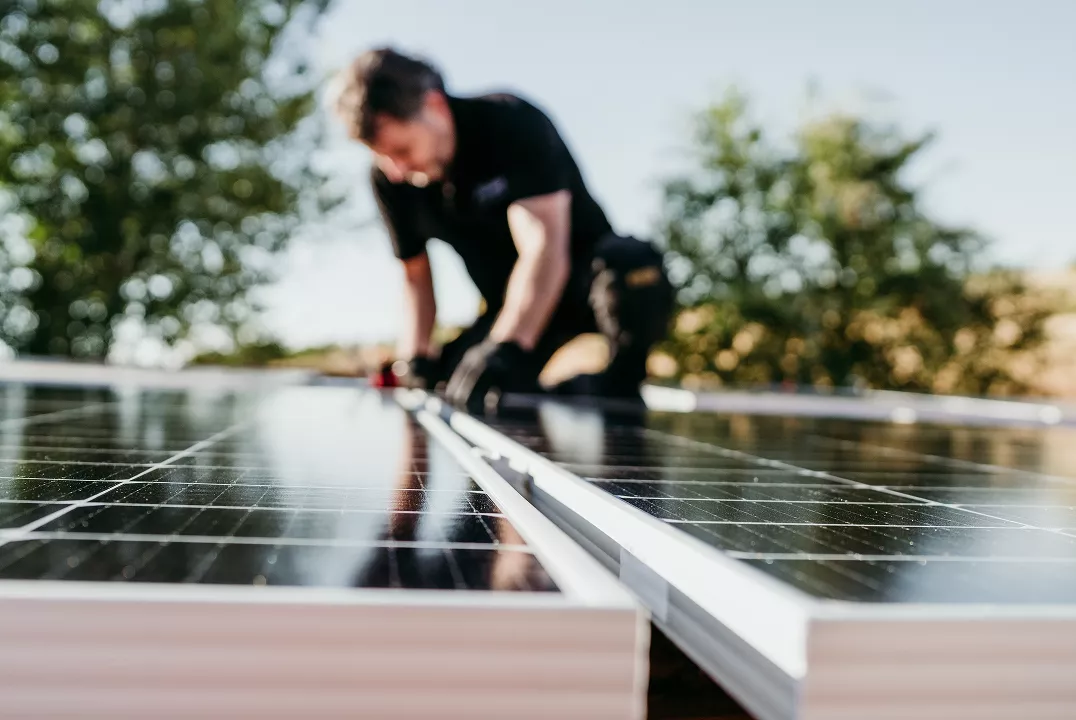 2ª. foto à direita superior Um homem de uniforme preto instala placas de energia solar sobre um telhado. 