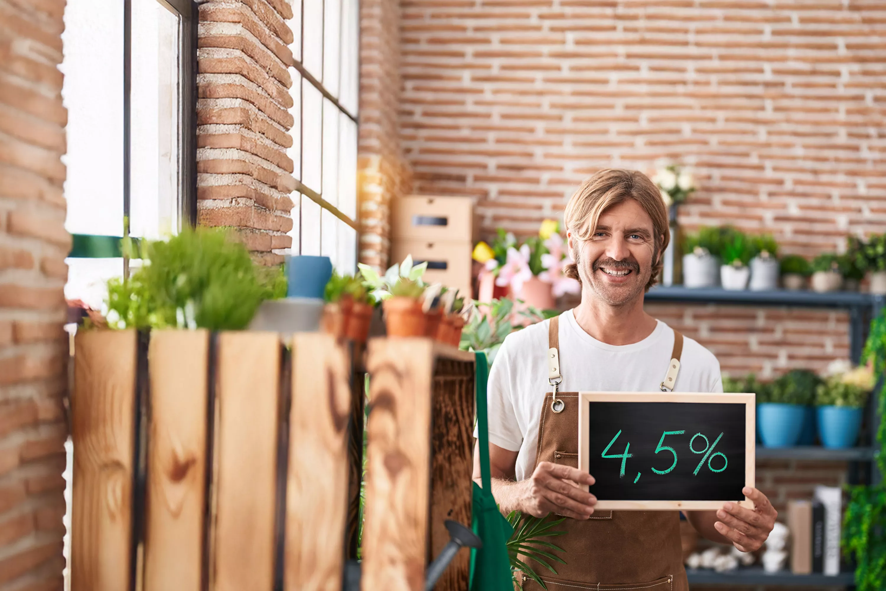 Zdjęcie pokazuje uśmiechniętego kwiaciarza w firmie z tabliczką 4,5%