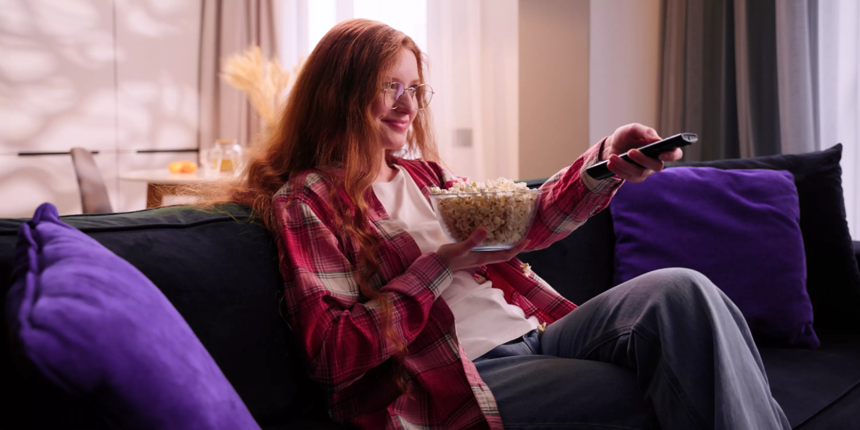 Szczęśliwa kobieta zasiada do seansu telewizyjnego na swojej kanapie.