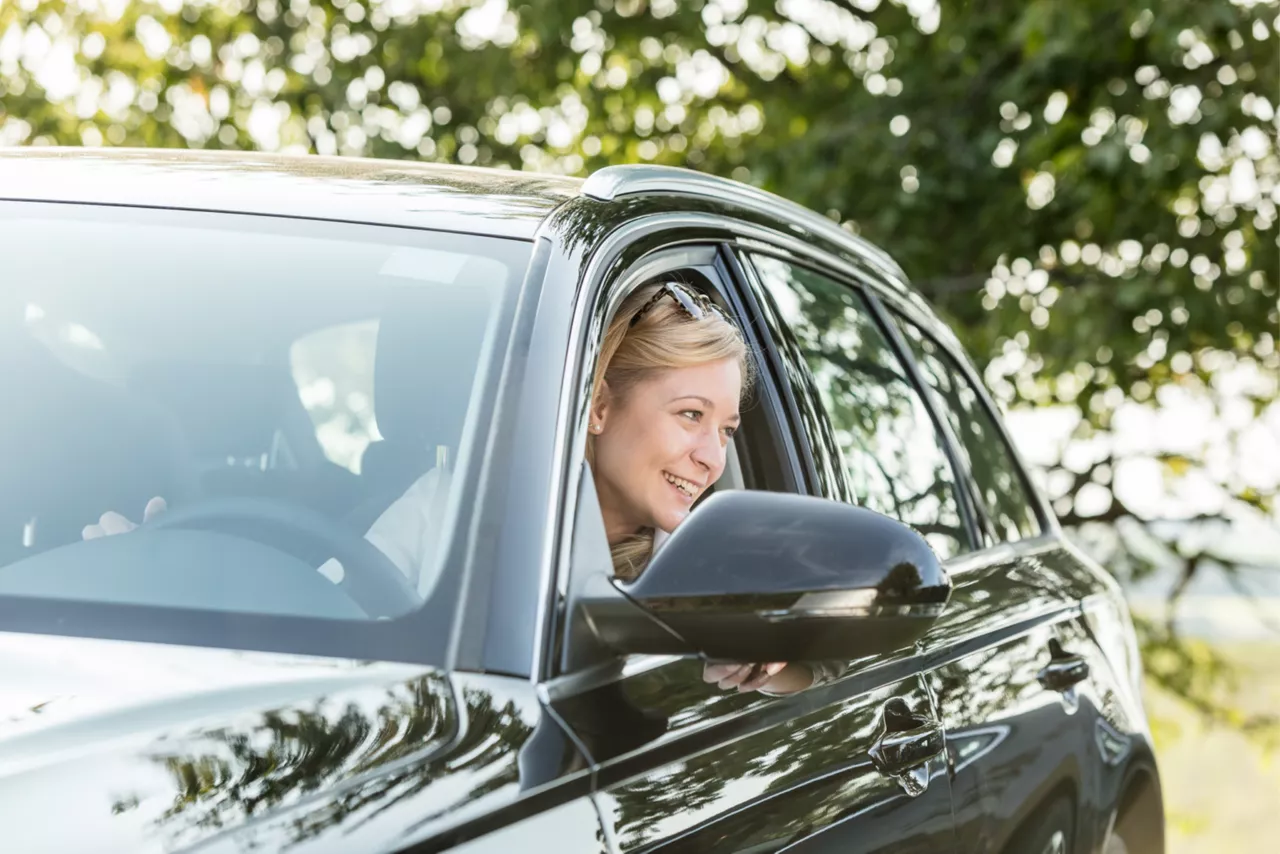 Mulher dentro de um carro. Ela está com o rosto na janela olhando para fora e sorrindo. 