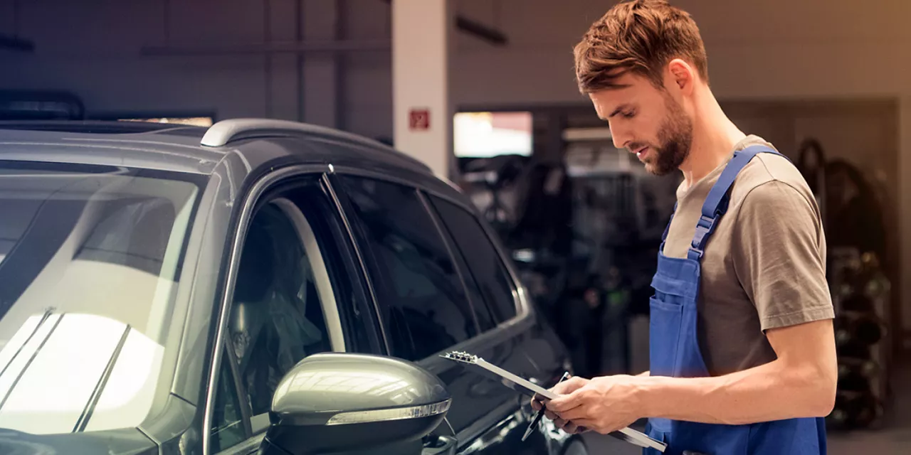 Revisões Planejadas Volkswagen: homem com prancheta parado em frente a um carro. 