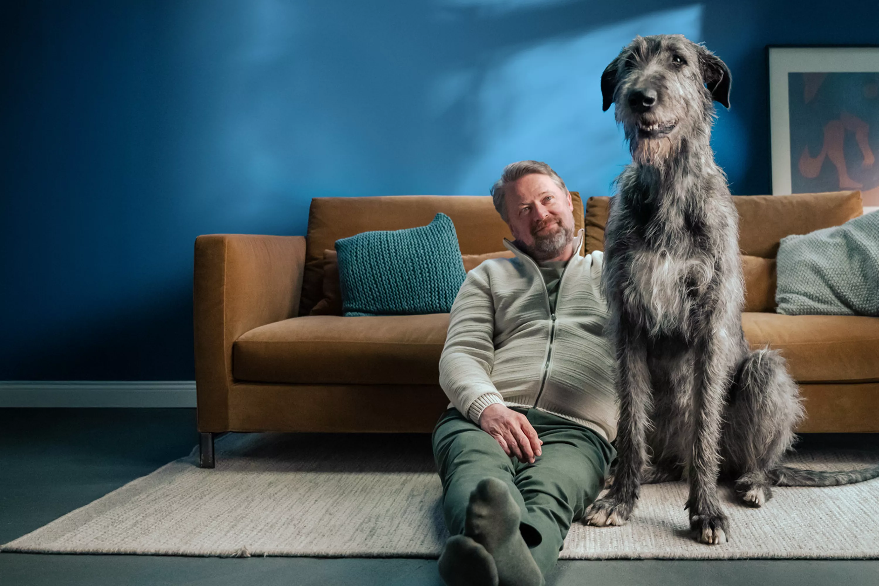Ein Mann und ein Hund vor einem Sofa.