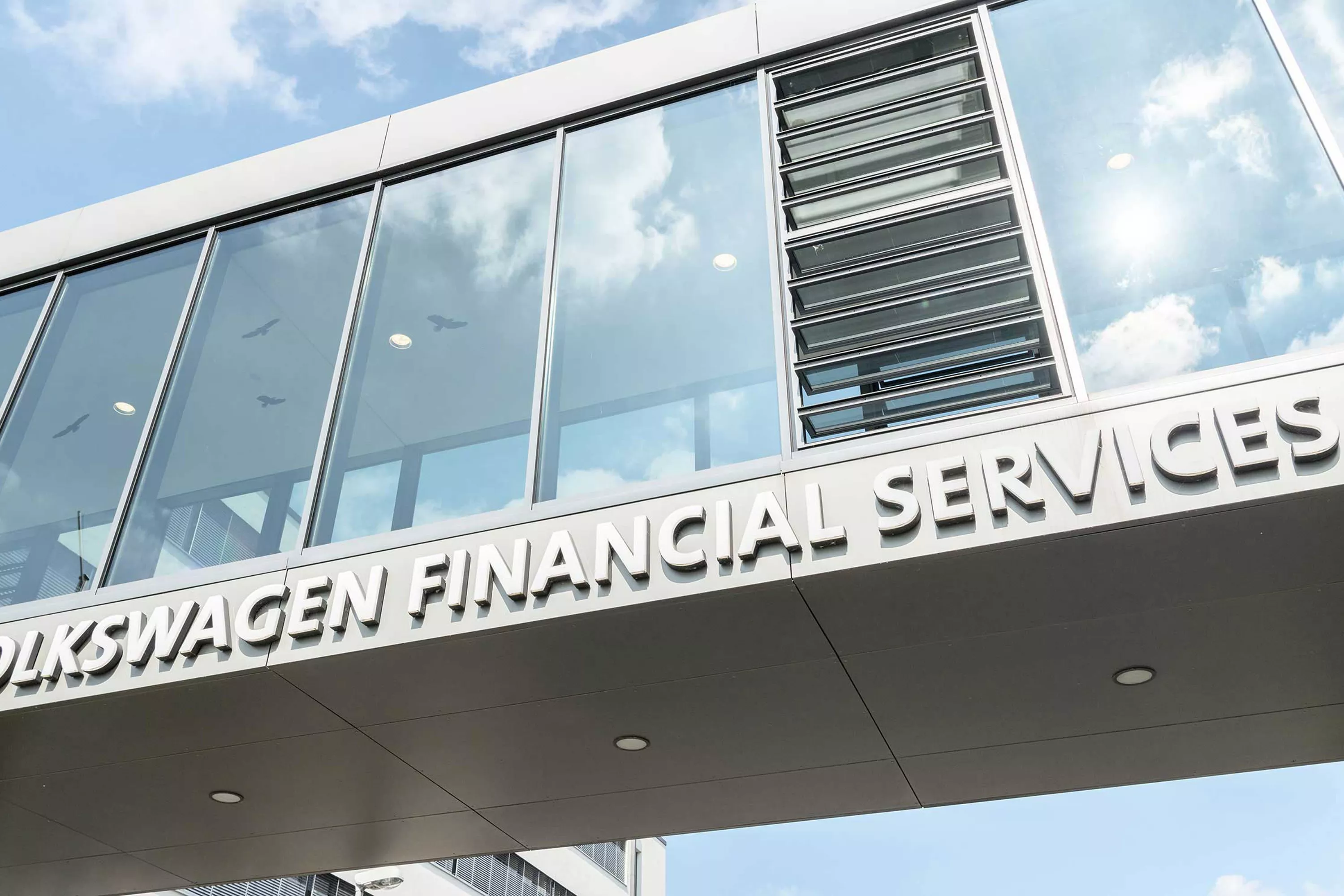 Szklany łącznik pomiędzy dwoma skrzydłami budynku z napisem "Volkswagen Financial Services"