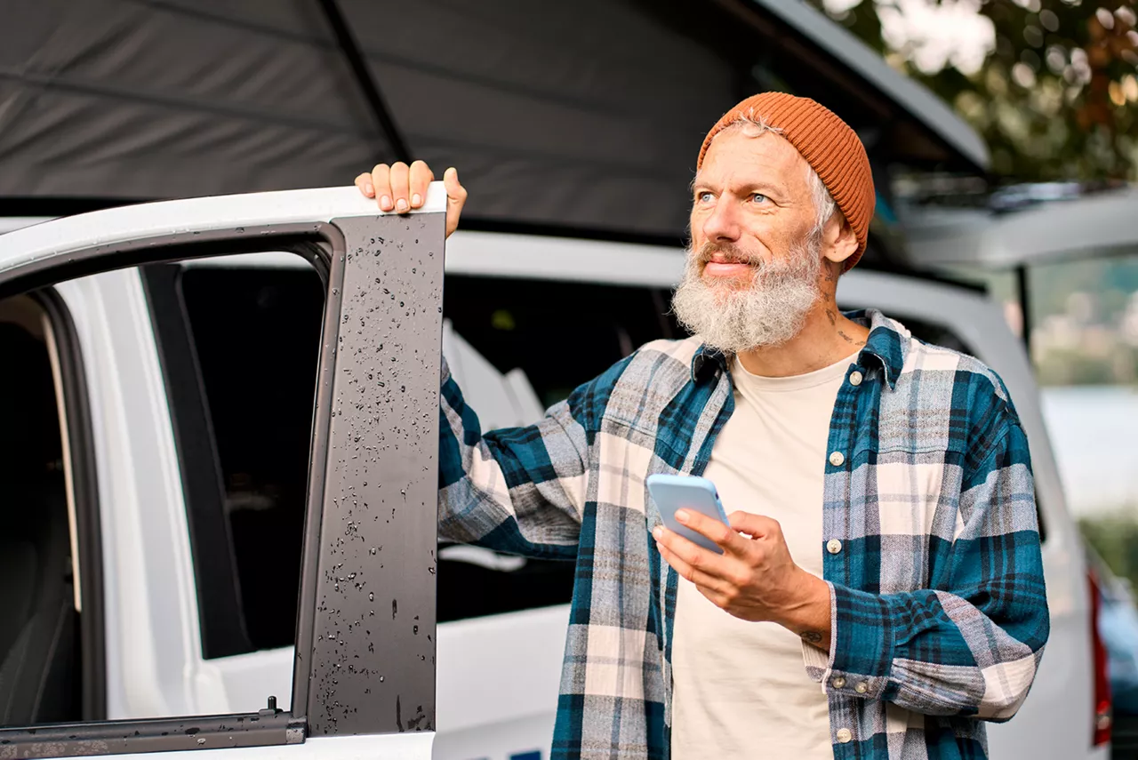Un hombre saliendo de un coche con un móvil en la mano