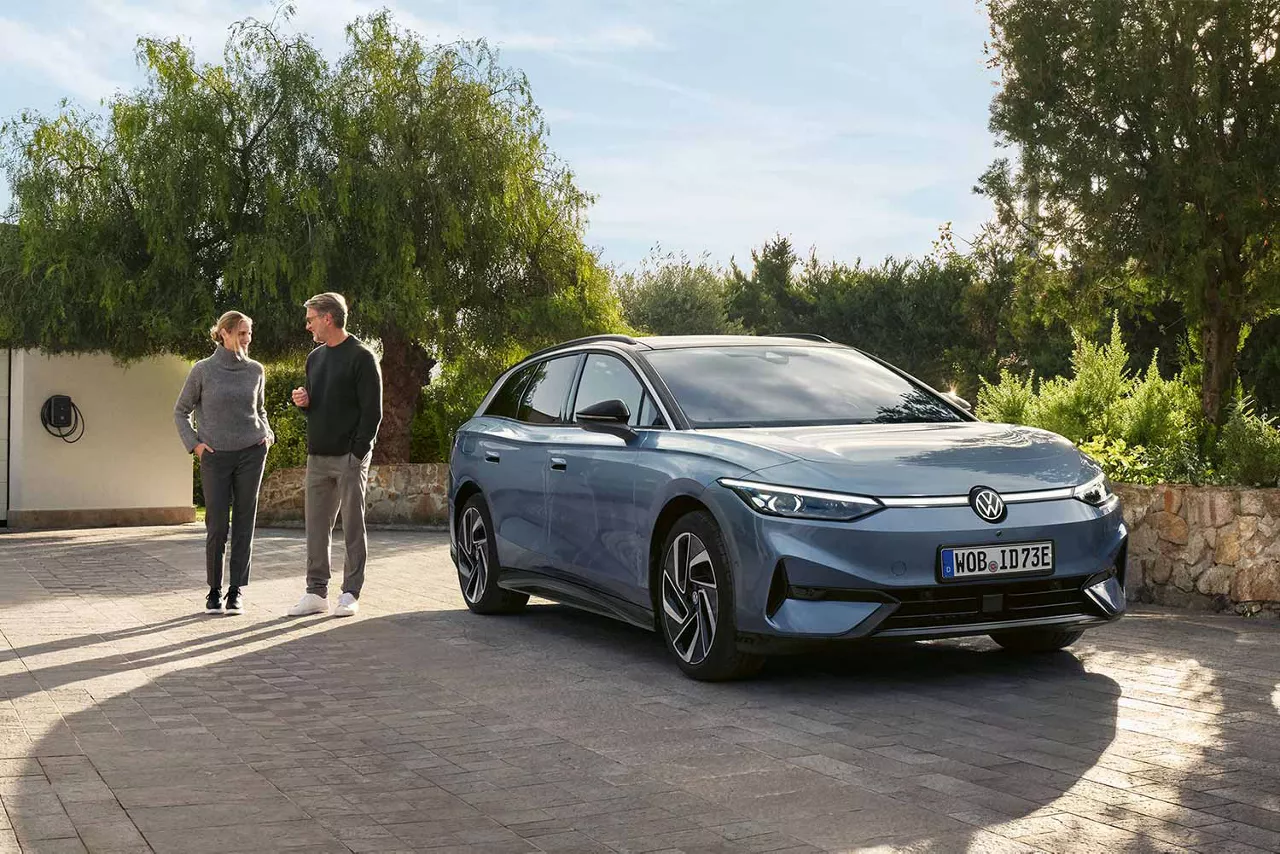 VW ID.7 Tourer auf einer Auffahrt mit einem Mann und eine Frau im Hintergrund