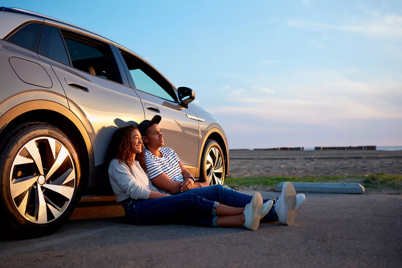 Una pareja sentada en el suelo apoyada en un coche del grupo Volkswagen FS