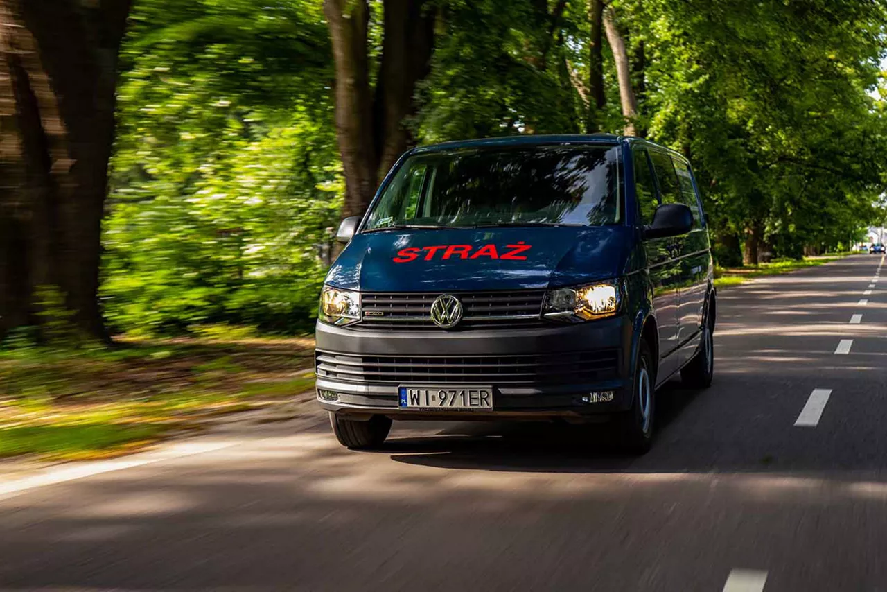 Volkswagen Transporter z napisem STRAŻ na drodze wśród drzew.