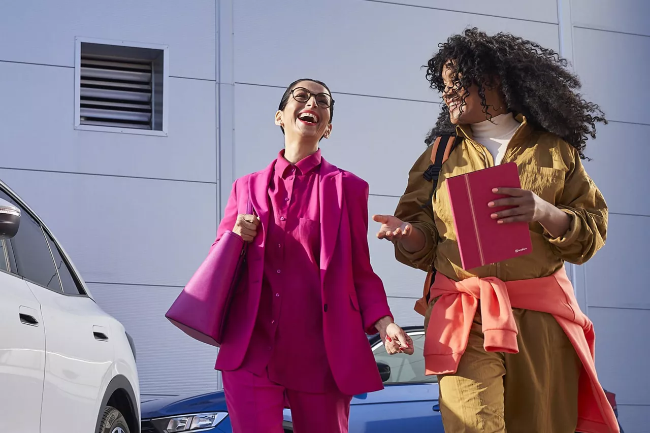 Dos chicas sonriendo caminando junto a un coche blanco de ofertas