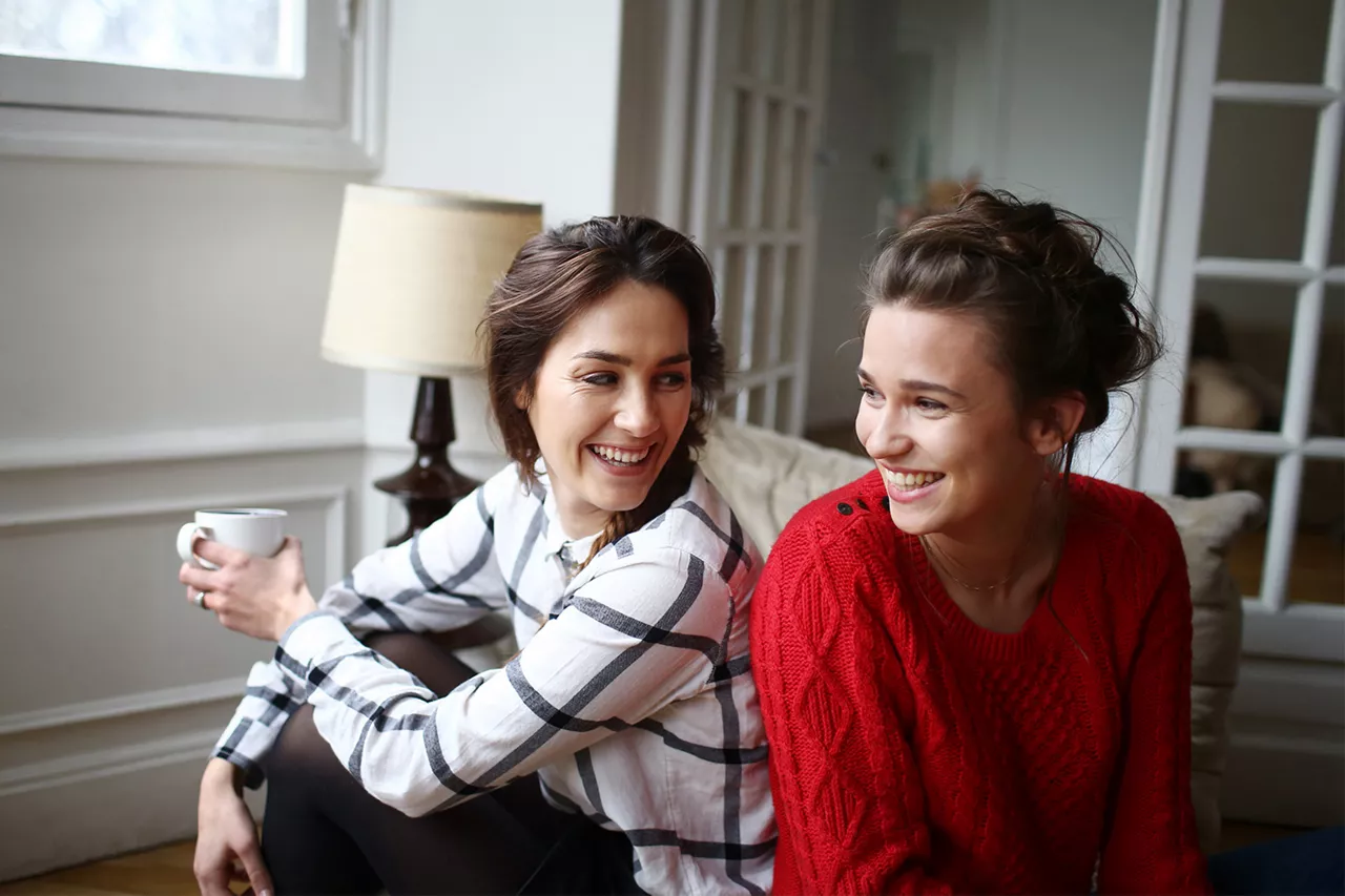 Dos chicas sentadas sonríen mientras una de ellas sostiene una taza