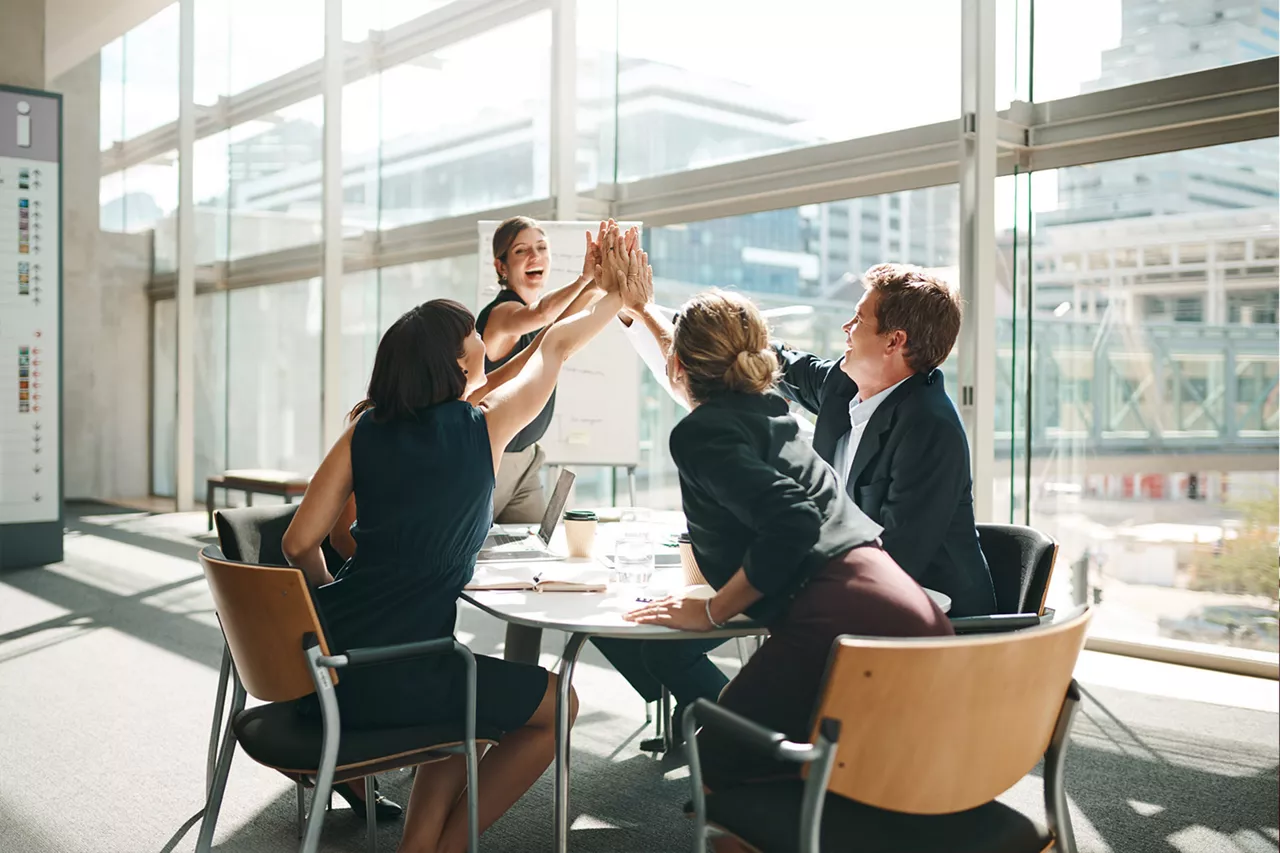 Grupo de personas entrono a una mesa de trabajo chocando las manos