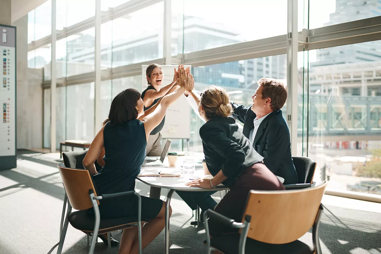 Grupo de personas entrono a una mesa de trabajo chocando las manos