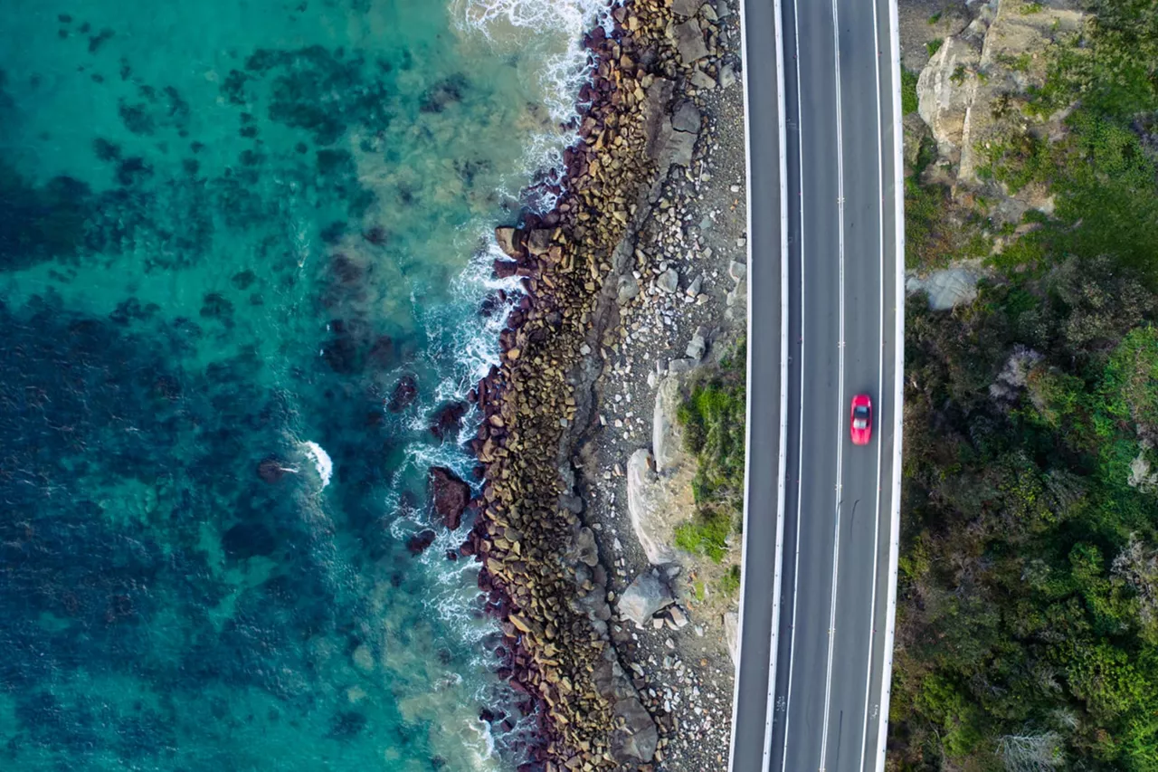 Un coche rojo en una carretera junto al mar visto desde arriba