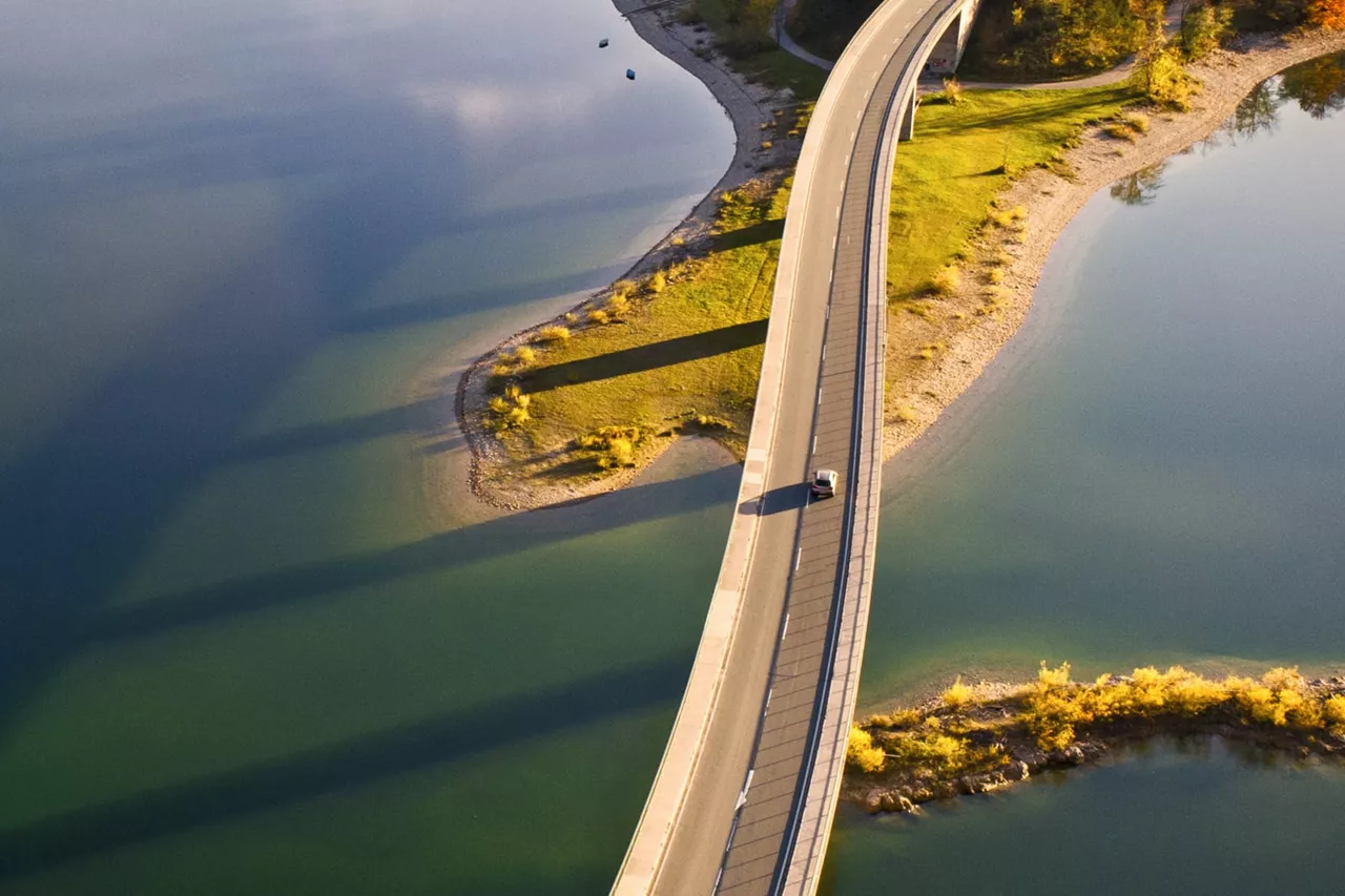 Un coche con Seguro de Automóvil visto desde arriba cruzando un puente al atardecer