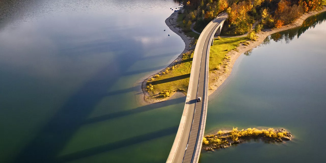 Un coche con seguro de coche visto desde arriba cruzando un puente al atardecer 