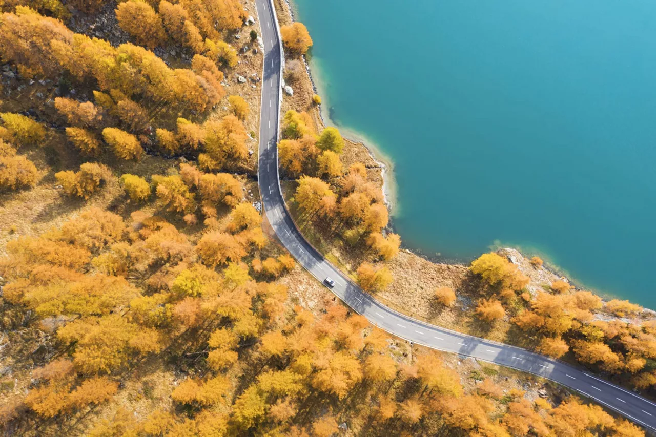 Un coche del Grupo Volkswagen visto desde arriba en una carretera otoñal junto a un lago