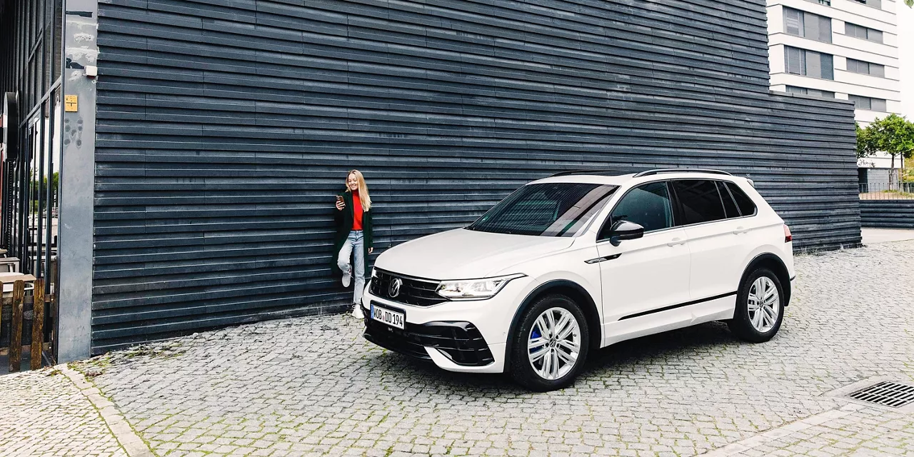 Volkswagen Tiguan visto de costado aparcado fretne a una fachada azul y una chica de pie