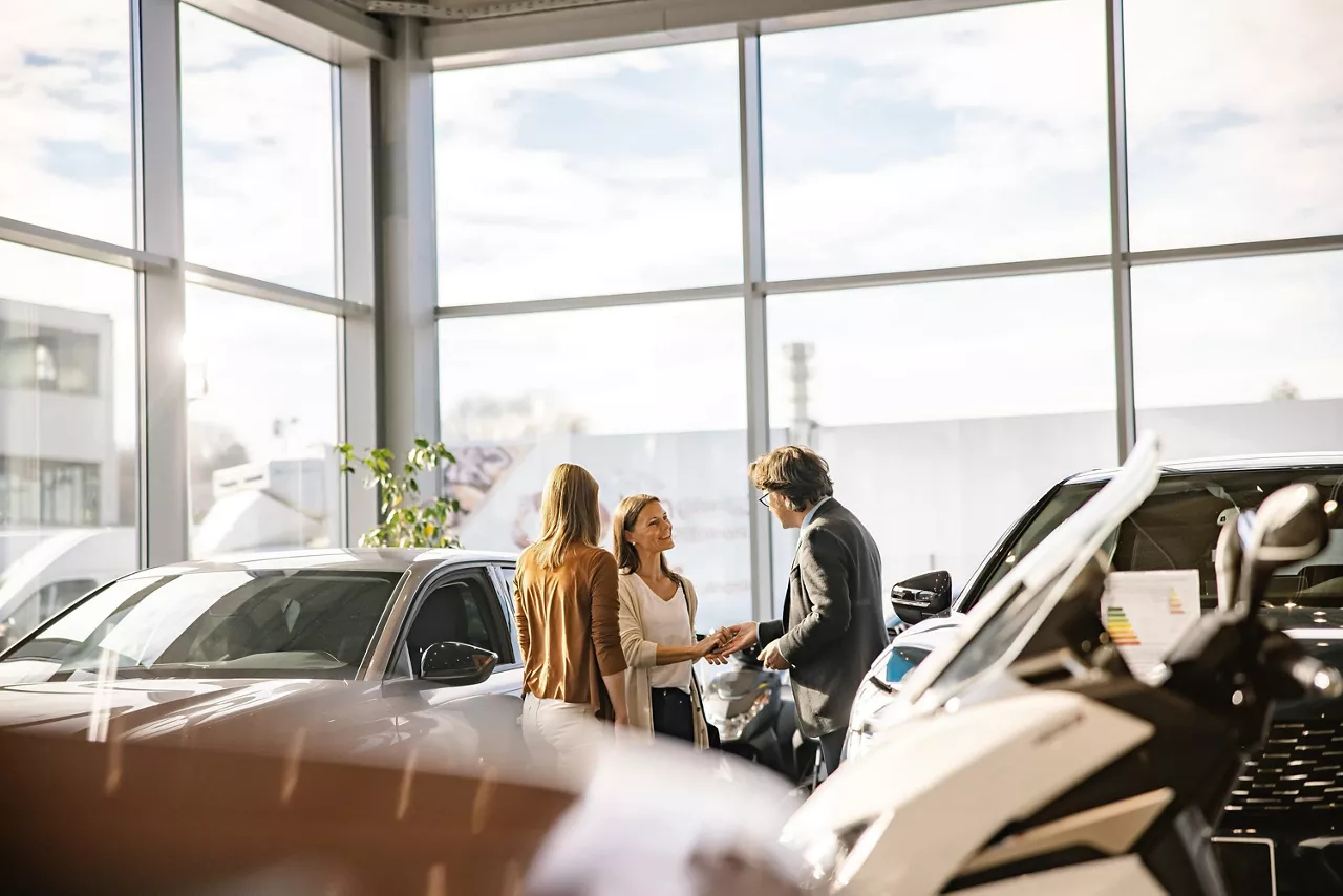 Dos mujeres hablan con un asesor comercial que les muestra un coche de renting empresas en un concesionario del Grupo Volkswagen