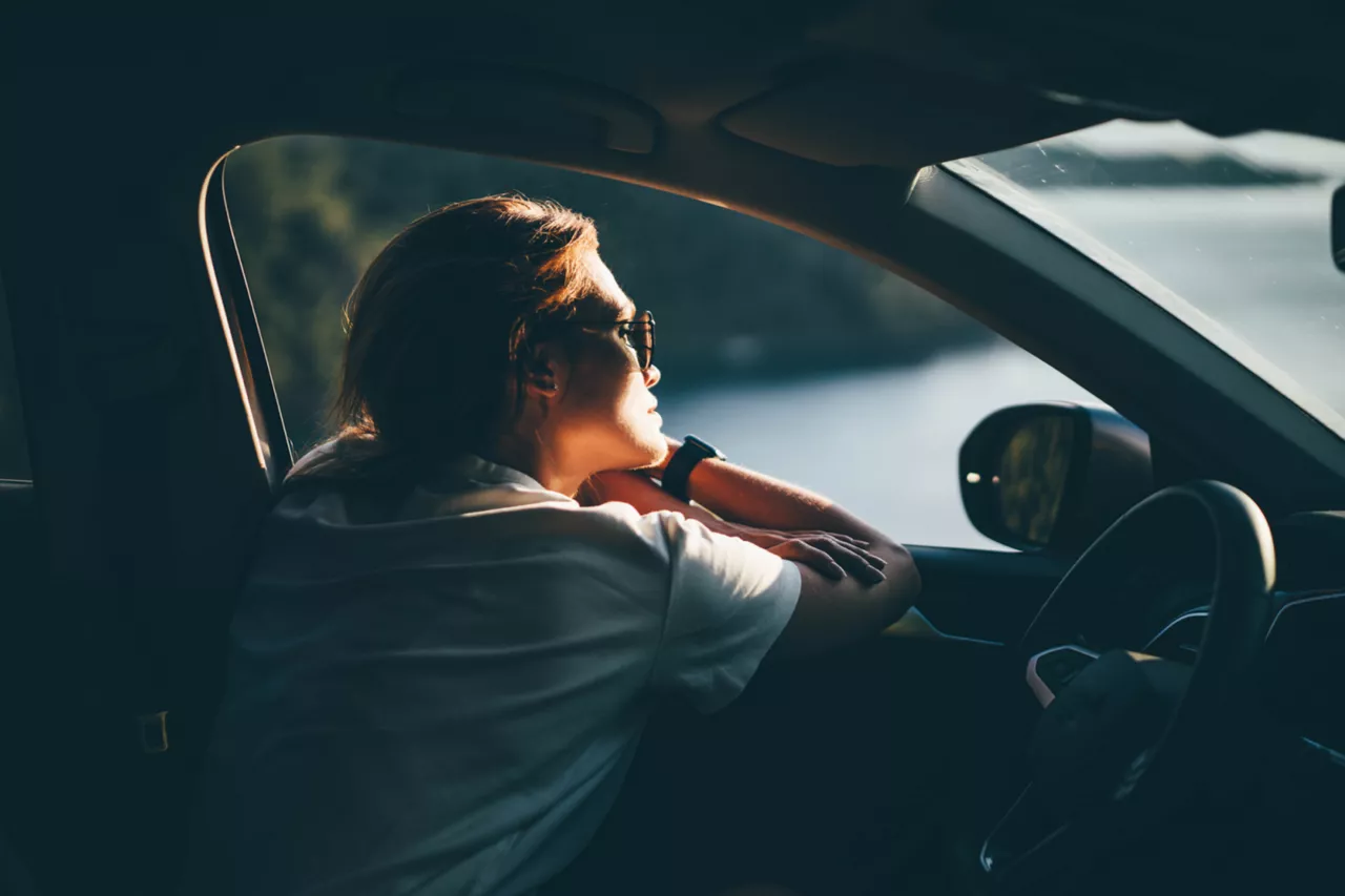 Una chica sentada dentro de un coche apoyada en la ventanilla mirando el exterior