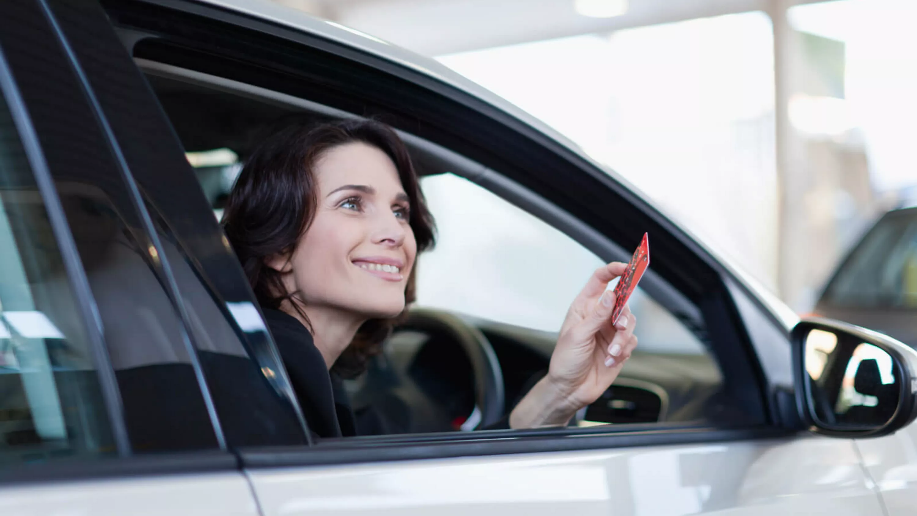 Plano medio de una mujer asomándose por la ventanilla de un coche eléctrico en un punto de recarga. 