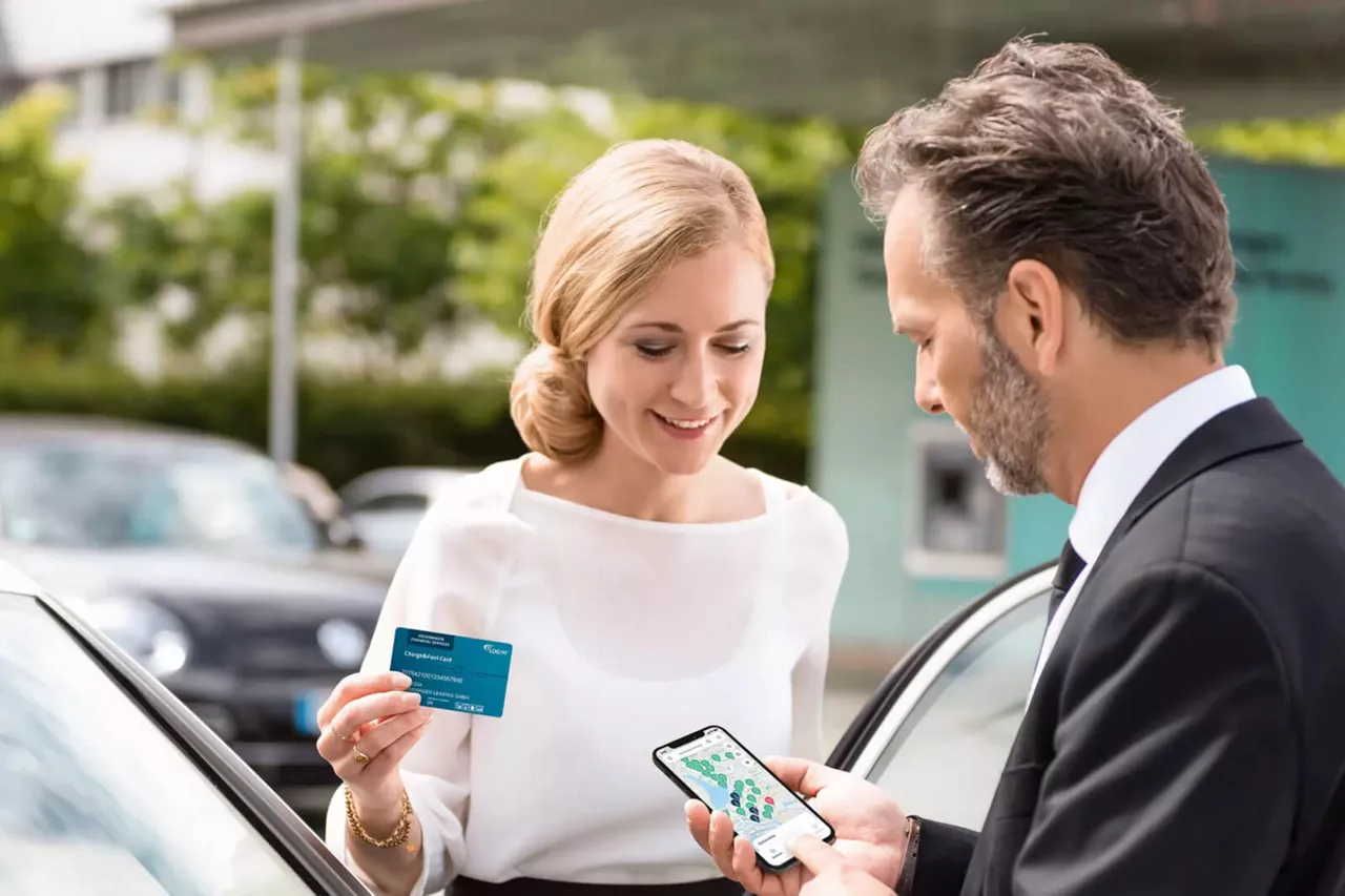 Dos personas con una trajeta de pago y una app en el móvil junto a un coche eléctrico del grupo Volkswagen