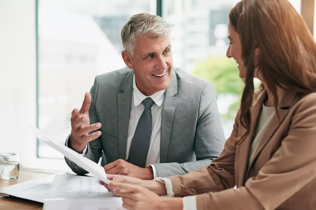 Dos personas hablando en una mensa con documentos en un concesionario, Renting para empresas