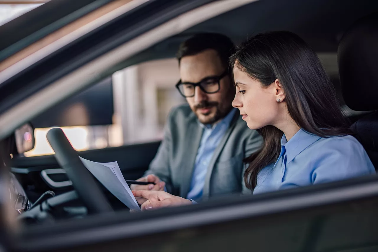 Una chica y un agente revisando un contrato sentados en un coche