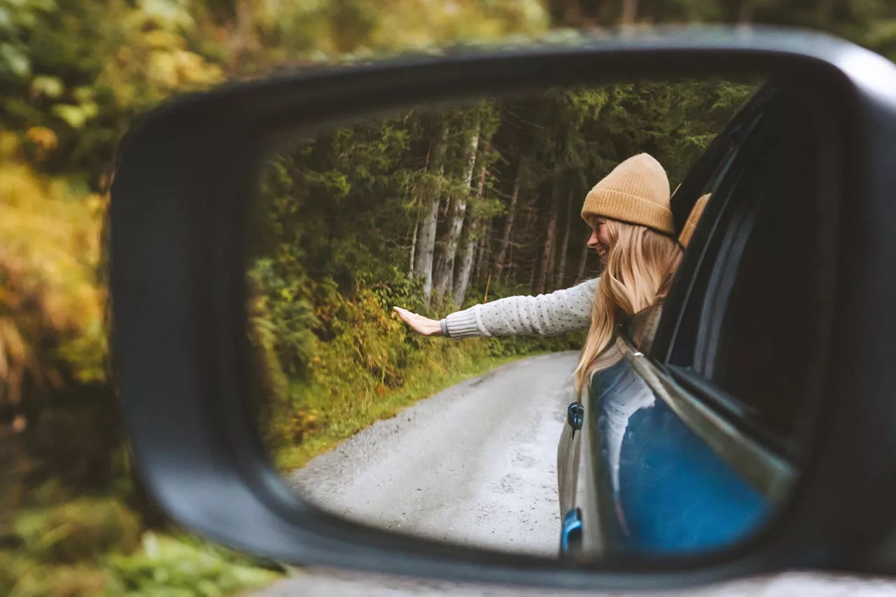 Una chica asomada por la ventanilla de un coche vista por el retrovisor