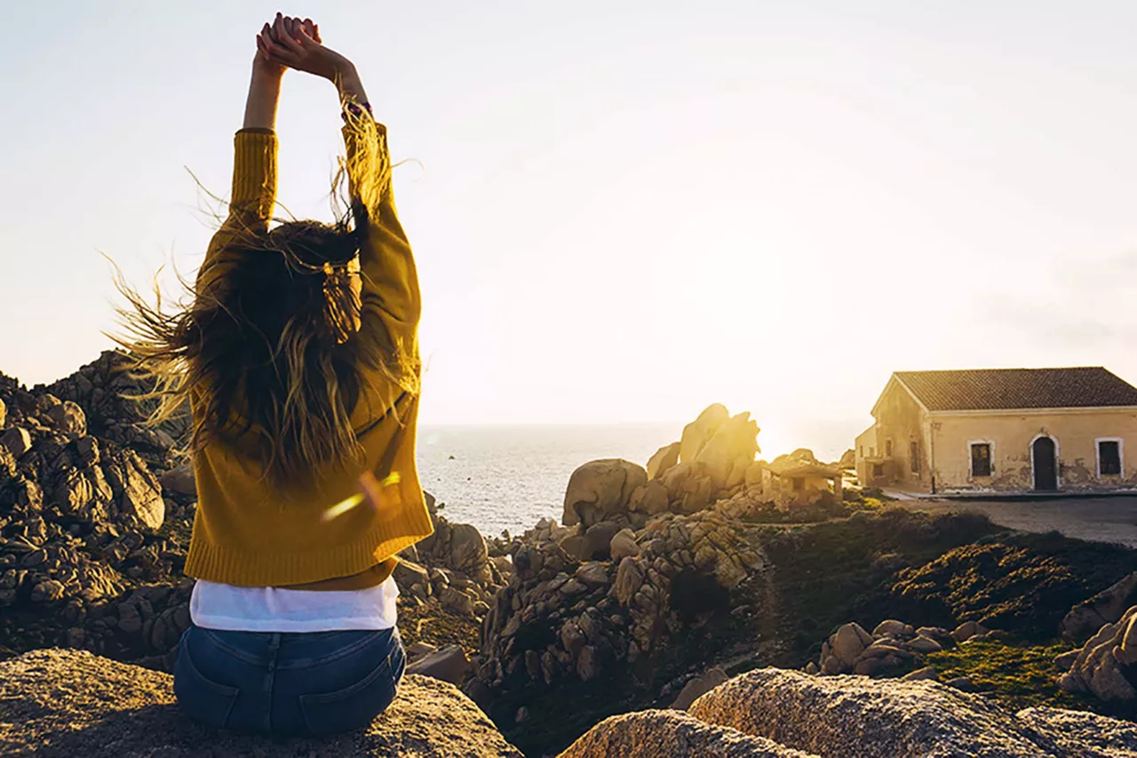 person-sitzt-auf-stein-und-hebt-hände-höhe-bei-blick-auf-meer