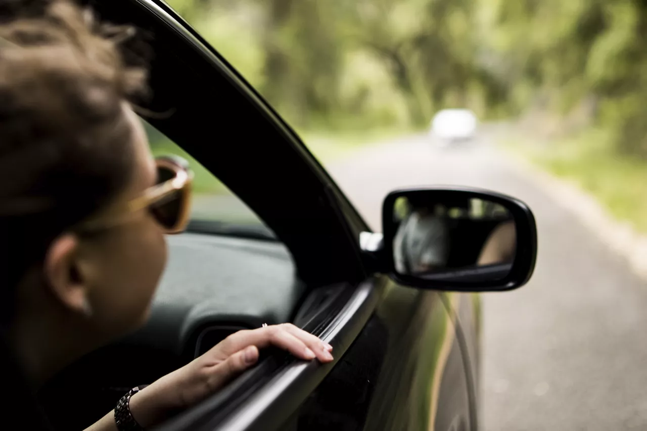 person-hält-während-der-fahrt-gesicht-aus-autofenster