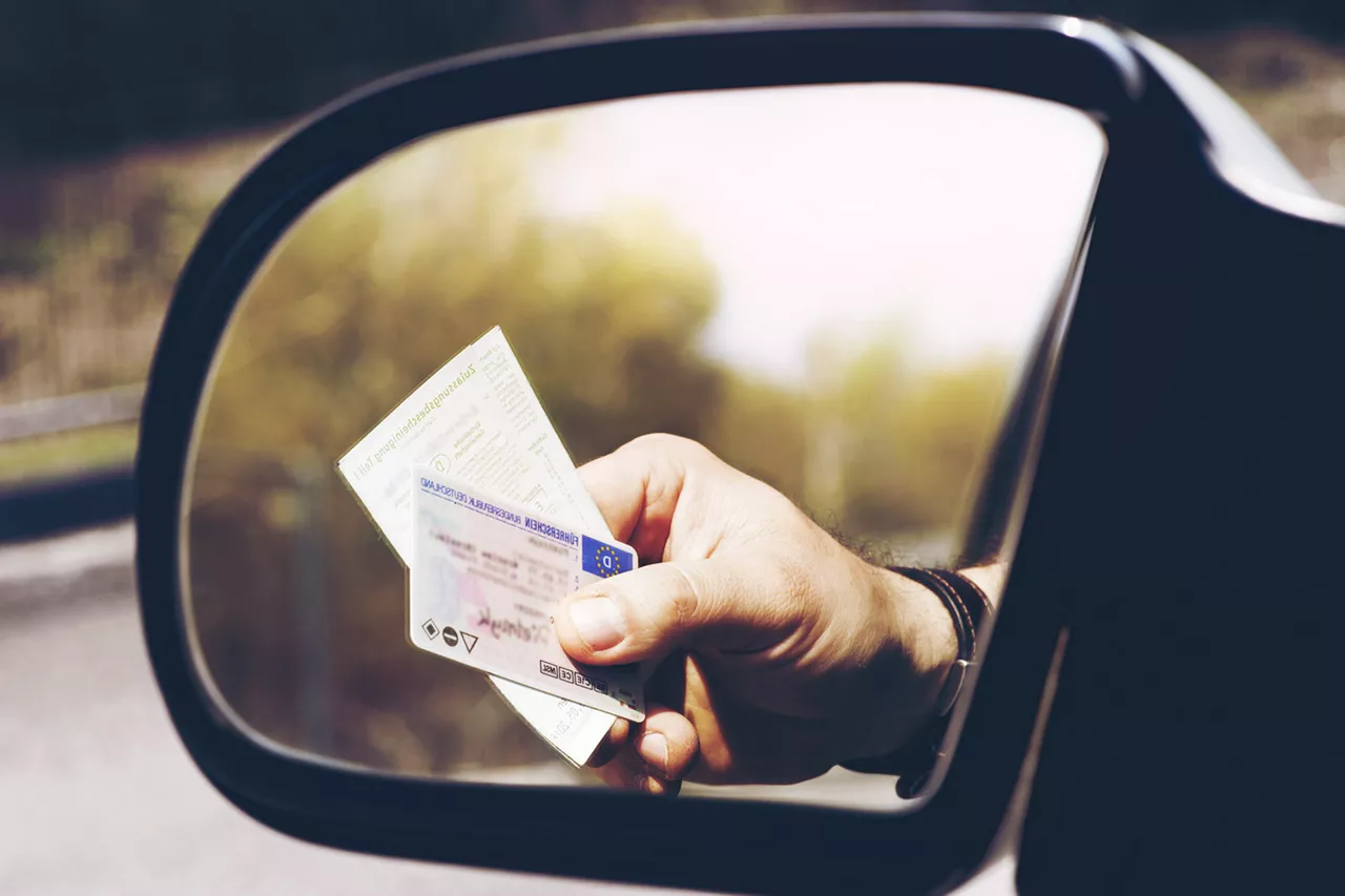 fahrer-eines-autos-hält-fahrzeugpapiere-aus dem-fenster