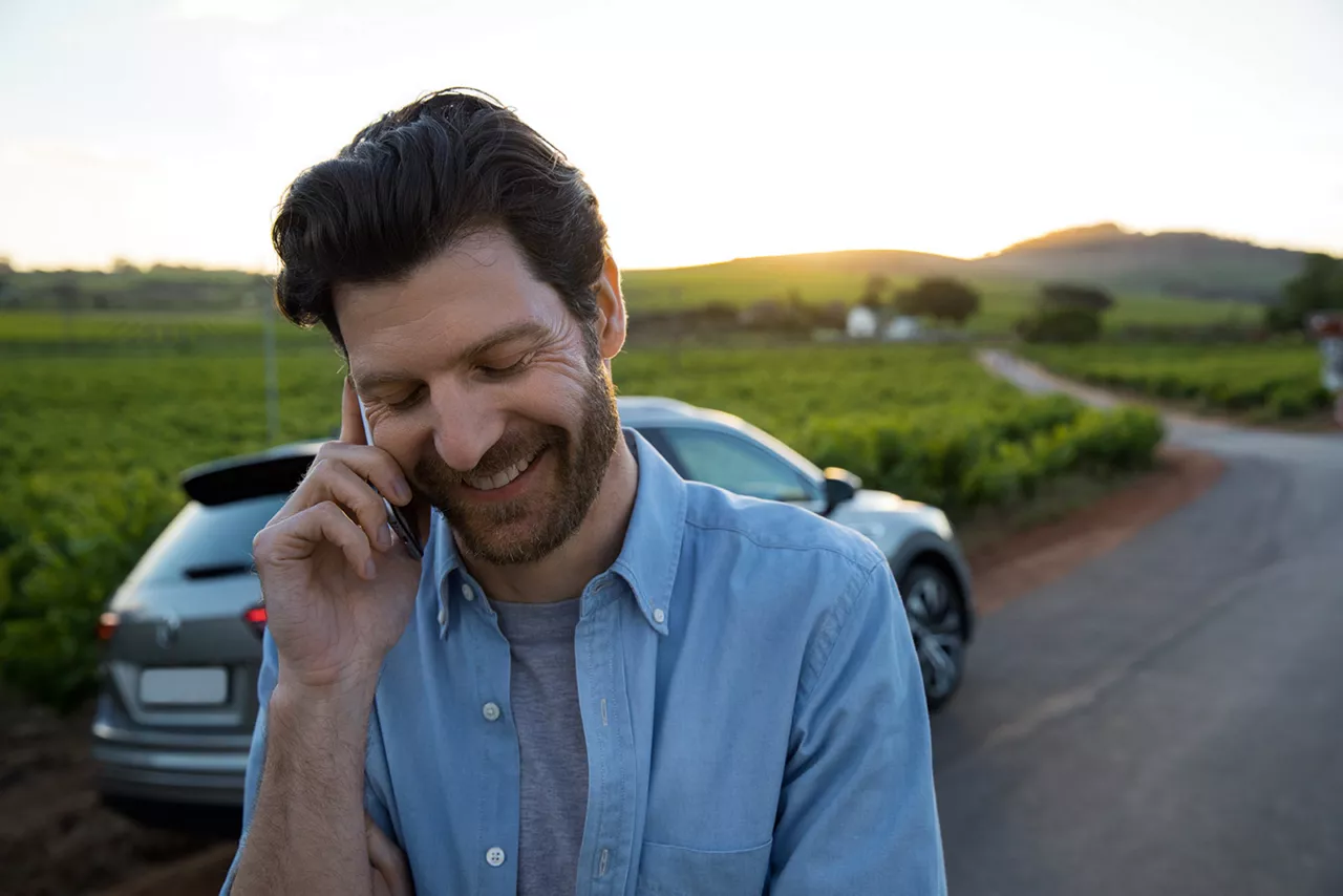 lächender-mann-am-telefon-und-auto-im hintergrund