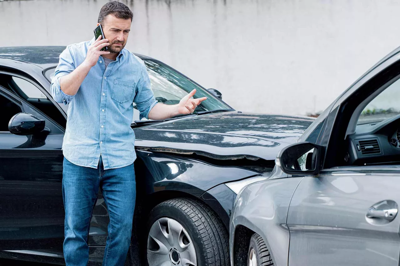 Person steht telefonierend und gestikulierend vor zwei kollidierten Fahrzeugen