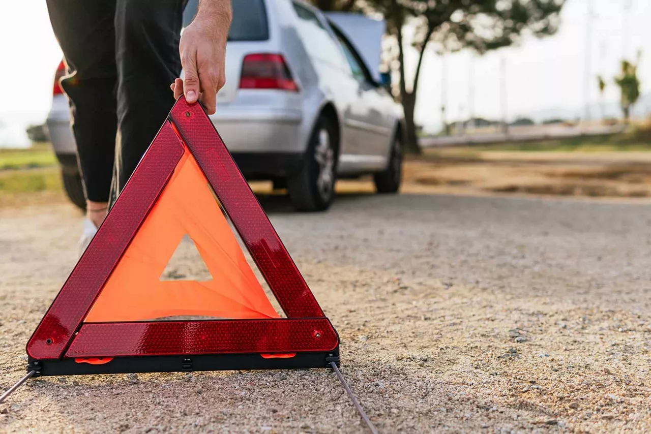 Person stellt ein Warndreieck hinter einem silbernen Auto auf