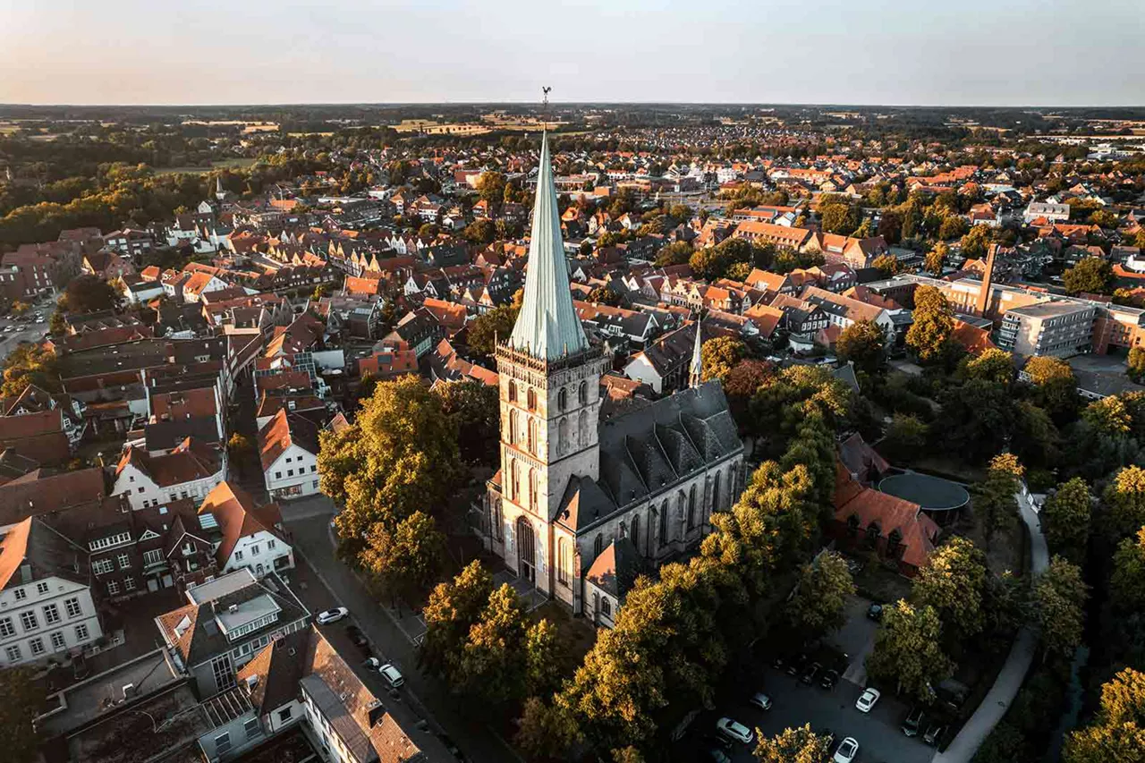 Luftaufnahme einer historischen Kirche mit hohem Turm in der Innenstadt von Lüdinghausen, umgeben von Wohnhäusern