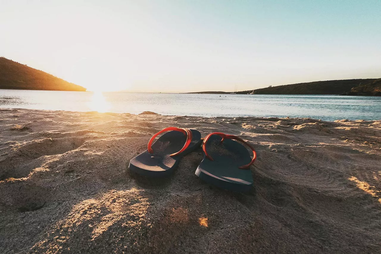 flip-flops-im-sand-am-meer-bei-sonnenuntergang