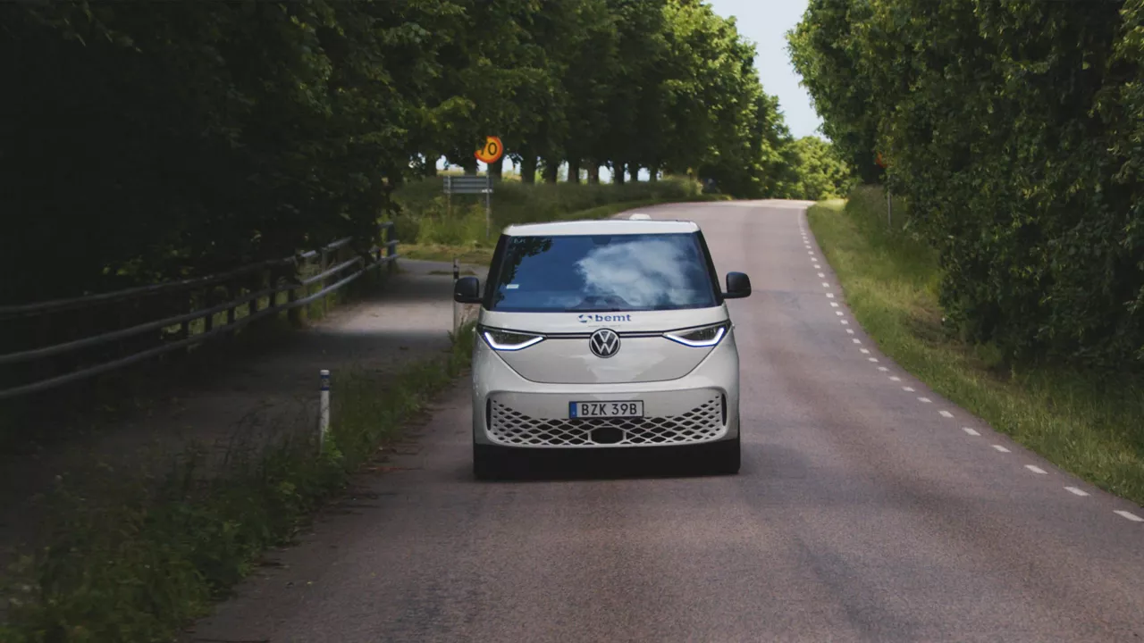 En bemt-profilerad Volkswagen ID. Buzz Cargo kör på en landsväg bland gröna träd.