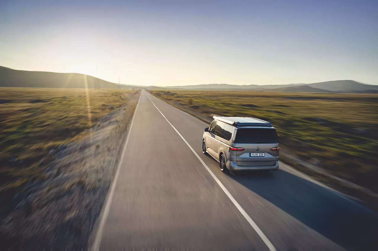 Ein Camper fährt auf einer langen, geraden Landstraße durch eine weite Landschaft bei tiefstehender Sonne.