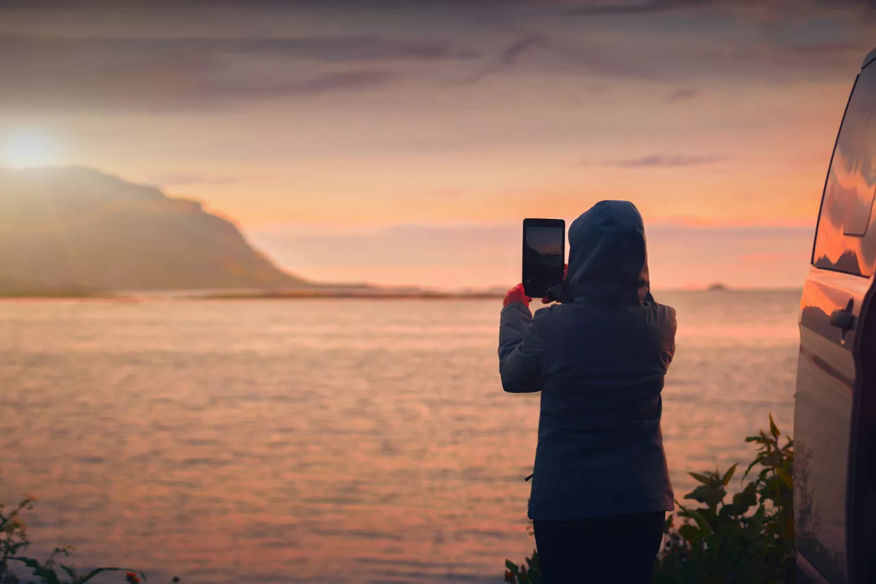 person-steht-neben-camper-und-fotografiert-sonnenuntergang-am-meer