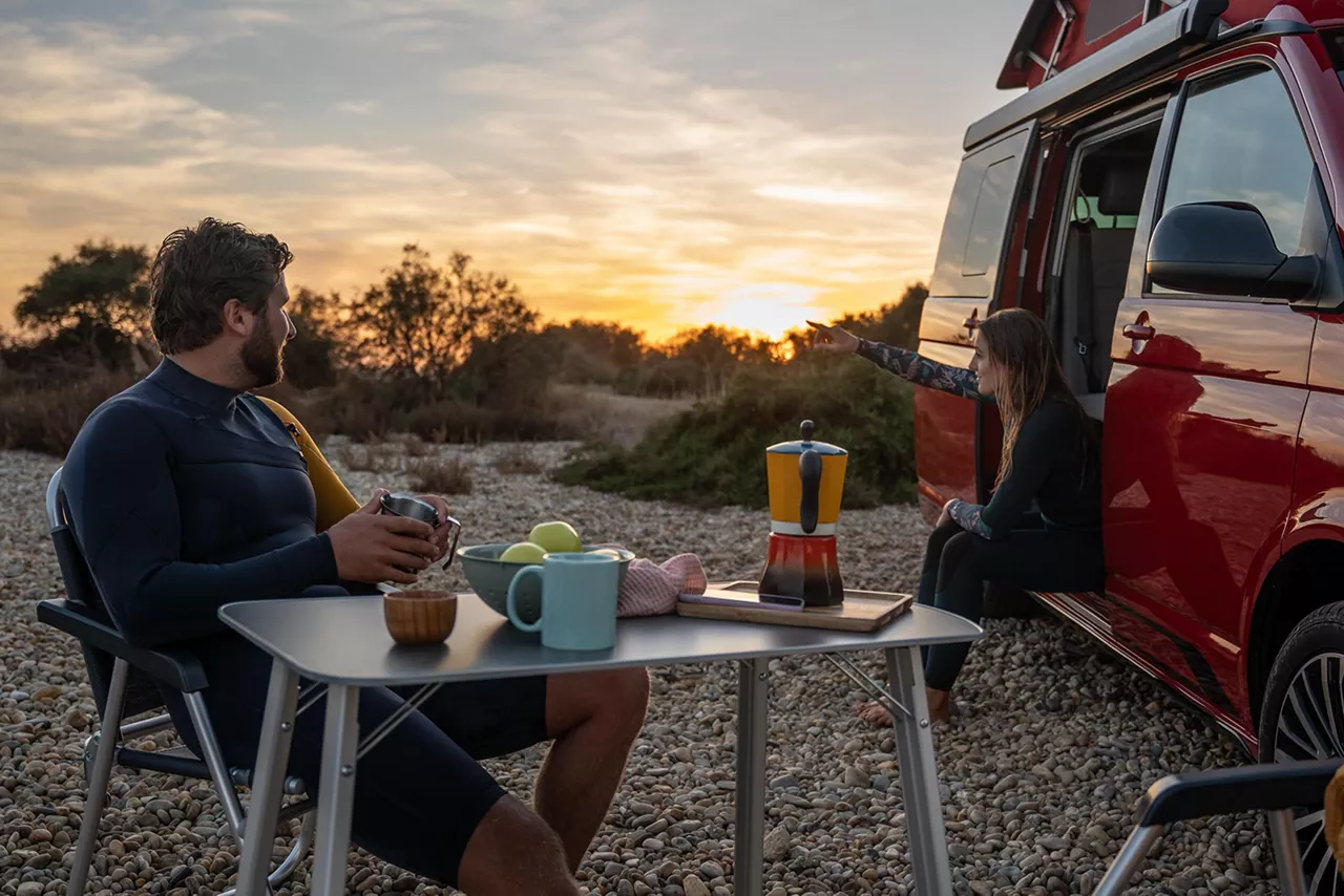 zwei-personen-sitzen-bei-sonnenuntergang-an-vw-california