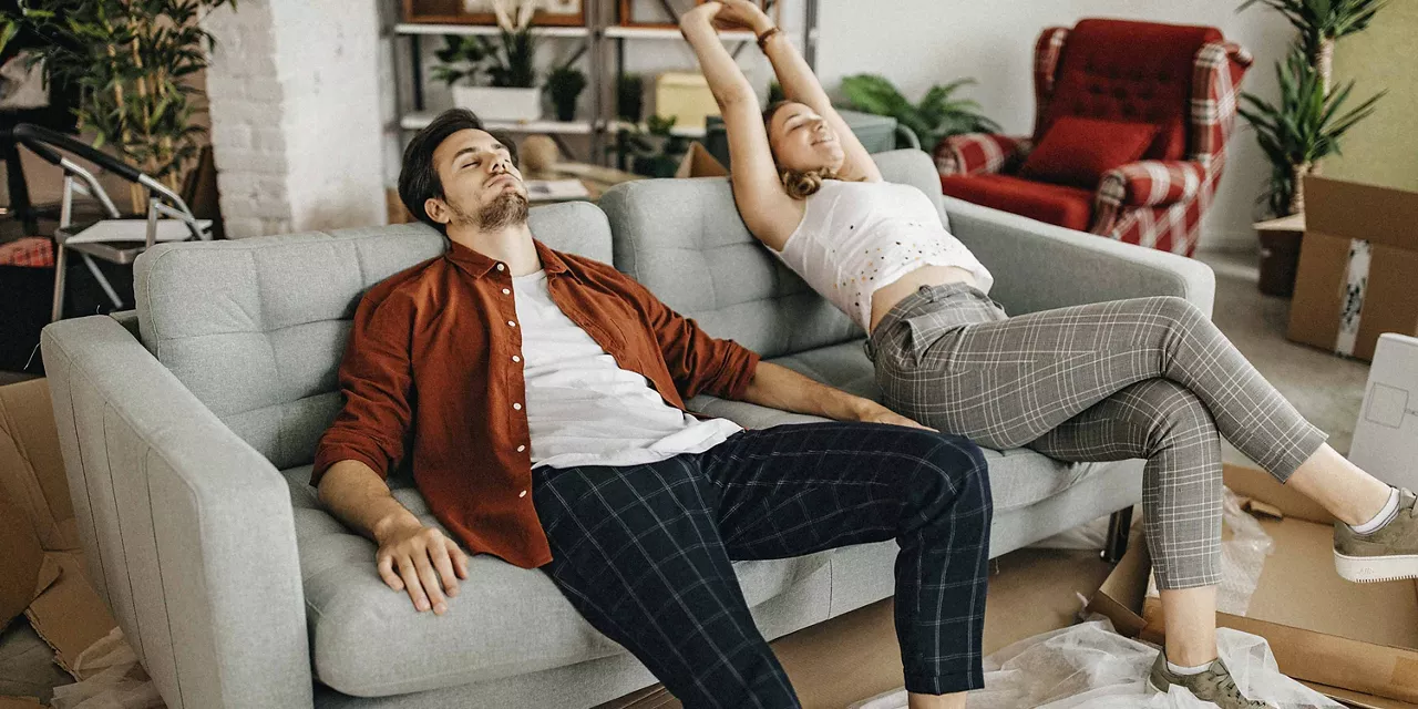 Zwei Personen sitzen erschöpft auf einem Sofa nach einem Umzug