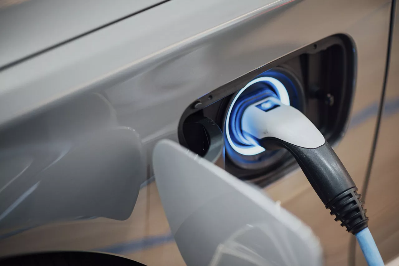 Nahaufnahme eines eingesteckten Ladekabels an der Ladebuchse eines silbernen Elektroautos