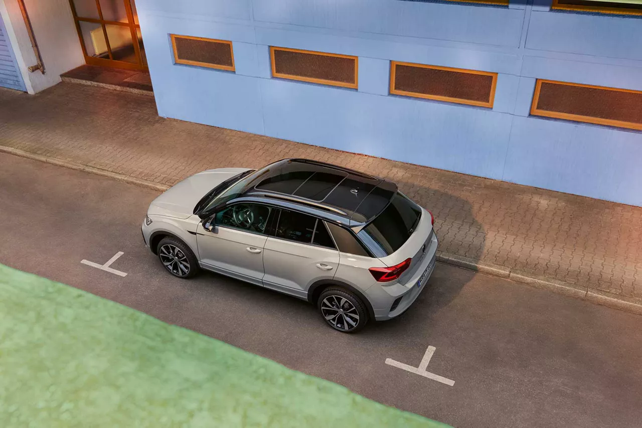 Beigefarbener VW T-Roc steht in einer Parkbucht vor bunten Gebäuden