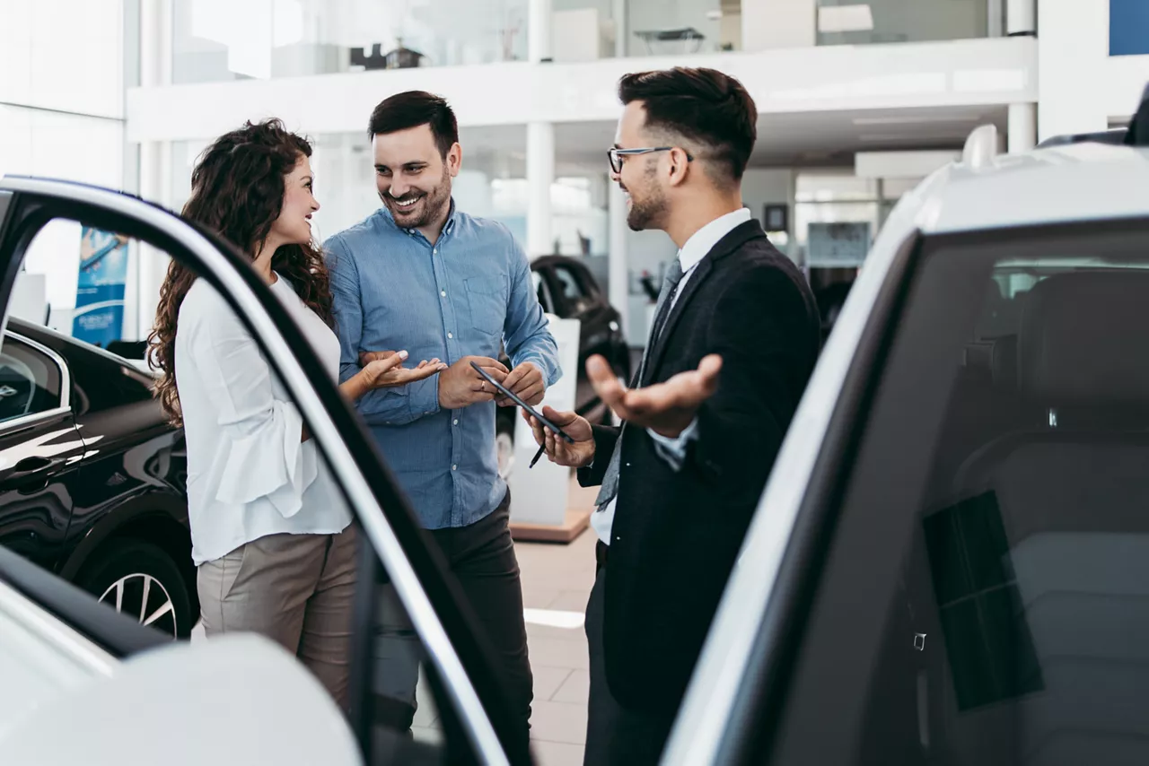 Berater erklärt zwei Personen ein Auto im Autohaus zwischen zwei Fahrzeugen.