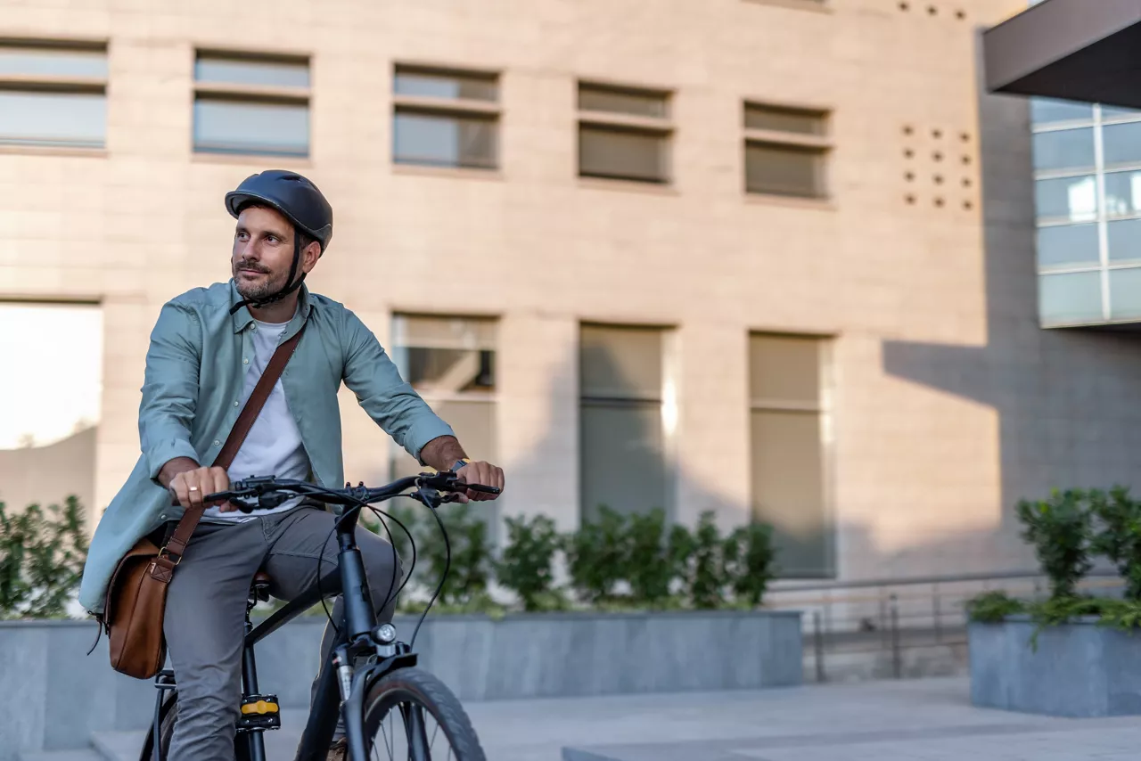 Mann mit Helm fährt auf einem Dienstrad durch die Stadt und ist unterwegs zur Arbeit