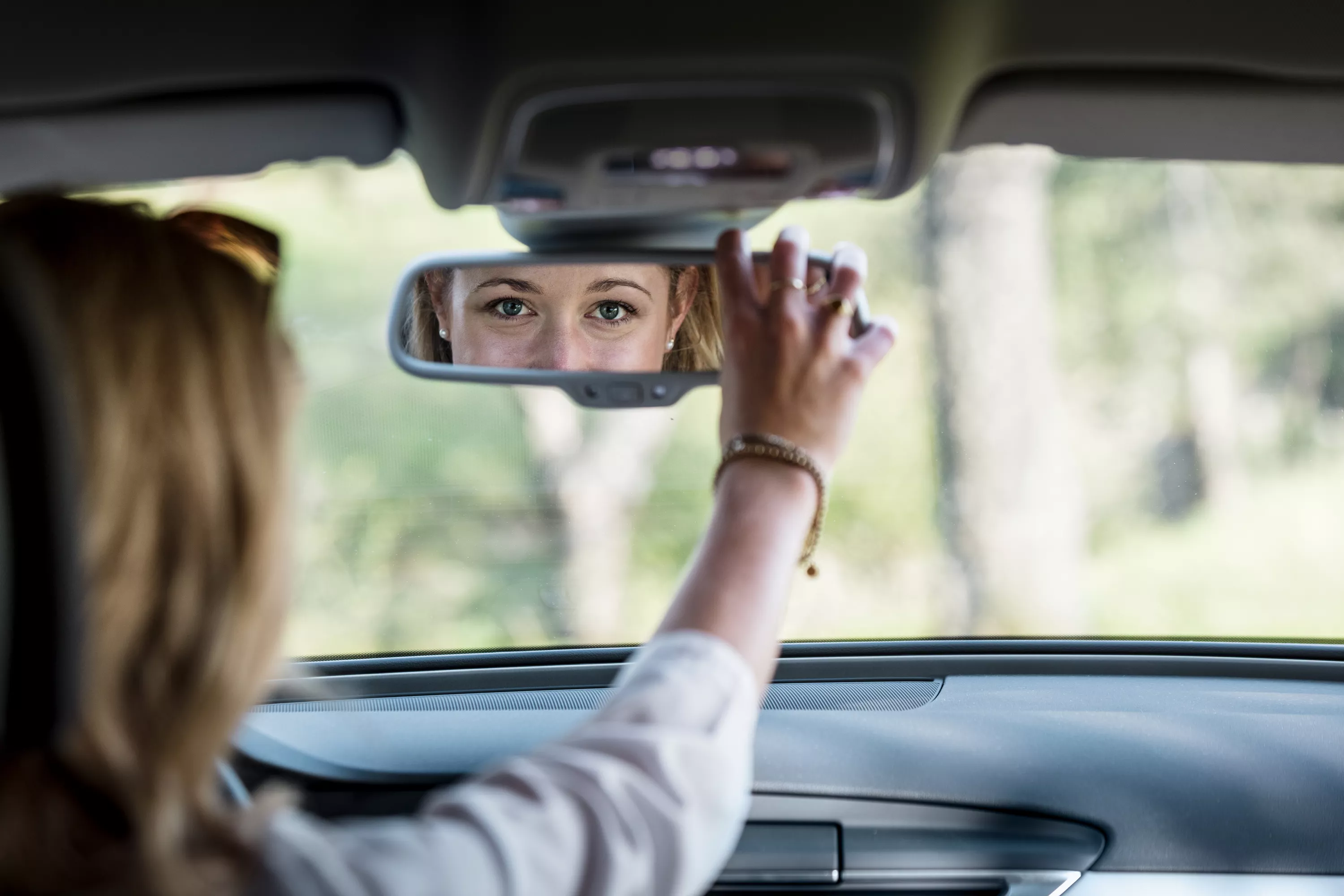 Blonde Frau blickt in den Rückspiegel.