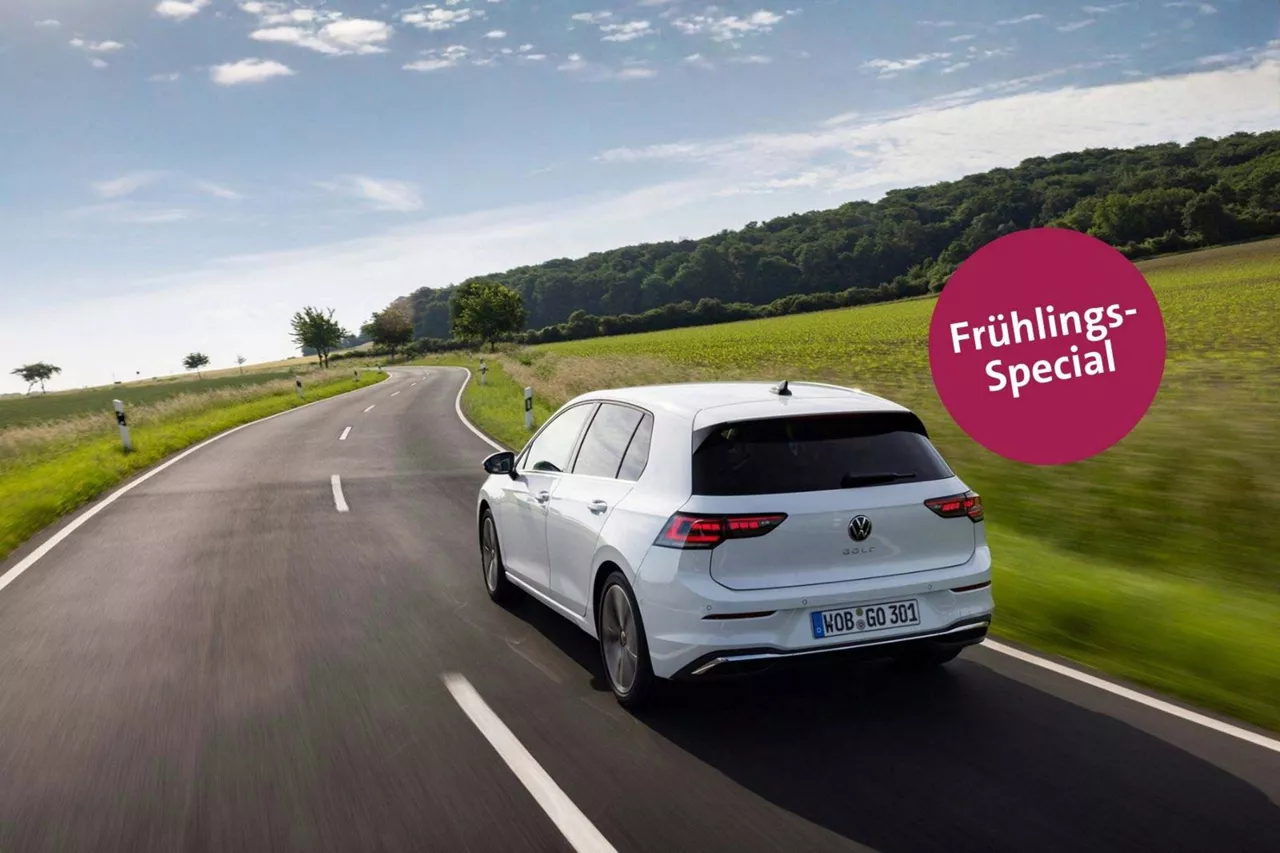 Weißer VW Golf fährt auf einer Landstraße unter blauem Himmel; Frühlings‑Special Hinweis eingeblendet.
