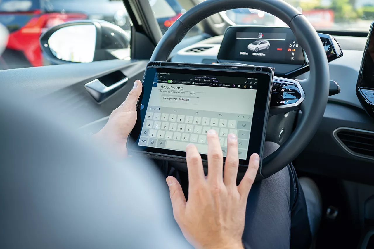 Nahaufnahme auf dem Fahrersitz. Eine Person tippt auf einem Tablet, das am Lenkrad angelehnt ist.